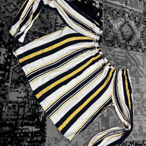 Randig offshoulder topp från Bershka - Snygg offshoulder topp från Bershka med randigt mönster i svart, vitt och gult. Toppen har långa ärmar och en elastisk kant upptill för en bekväm passform. Perfekt för en trendig look!