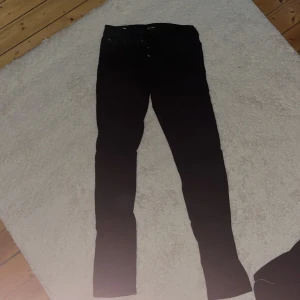 Svarta jeansbyxor - Snygga svarta jeansbyxor med en slim passform. De har en klassisk design med knappar och dragkedja framtill. Perfekta för en stilren look.