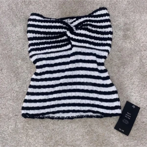 Randig stickad tubtopp från NAKD - Snygg randig tubtopp från NAKD i svart och vitt. Toppen är stickad och har en twistdetalj framtill som ger en unik look. Perfekt för en stilren outfit.