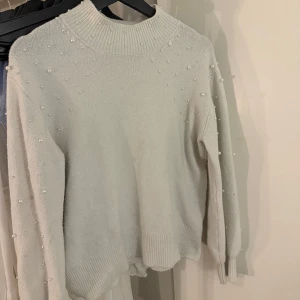 Vit tröja med pärlor från Kappahl - Säljer en stilren vit tröja från Kappahl dekorerad med pärlor över axlar och ärmar. Tröjan har en hög krage och långa ärmar, perfekt för en elegant look. Den är mjuk och bekväm, idealisk för kyligare dagar. Passa på att köpa denna fina tröja! 🤍Inga knappar borta i väldigt fint skick!❣️ en varm tröja med inte så hög krage