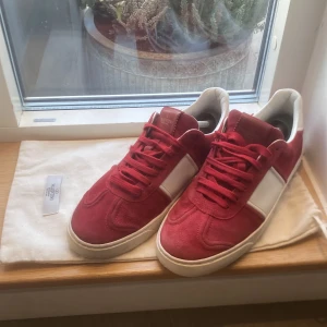 Röda valentino flycrews  - Snygga röda sneakers i mocka med vita detaljer och nitar på sulan. Skorna har snörning och en stilren design som passar perfekt för en trendig look. Storlek 41