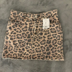 Leopardmönstrad jeanskjol - Trendig leopardmönstrad jeanskjol från Gina tricot med lappen kvar. Kjolen har en klassisk femficksdesign och stängs med knapp och dragkedja.
