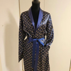 Mönstrad morgonrock i blått - Snygg blå morgonrock med ett lyxigt mönster i guld. Rocken har långa ärmar och ett matchande bälte i midjan. Perfekt för att chilla hemma med stil.