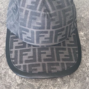 Grå keps från Fendi - Snygg grå keps från Fendi med ett distinkt mönster i svart. Kepsen har en justerbar rem baktill för perfekt passform. Perfekt för att ge en stilren touch till din outfit.