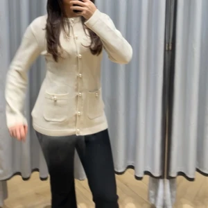 Beige kofta med pärldetaljer - Säljer en elegant beige kofta med pärldetaljer och knappar framtill. Koftan har långa ärmar och två praktiska fickor. Perfekt för en stilren look.