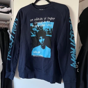 Sweatshirt med Håkan Hellström-tryck - Säljer en marinblå sweatshirt med ett stort blått tryck av Håkan Hellström på framsidan och texten 'Om kärlek va skepp skulle du ha tusen vrak i dig'. Ärmarna har blå text med 'Hellström'. Perfekt för fans av Håkan! 💙 Använd en handfull gånger. Önskar du veta exakta mått? Tveka inte att höra av dig!