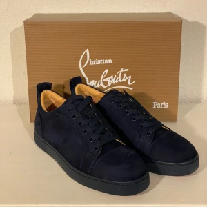 Mörkblå Christian Louboutin - Snygga mörkblå sneakers från Christian Louboutin i mocka med den ikoniska röda sulan. Skorna har snörning och en stilren design som passar perfekt för en trendig look. Levereras med originalförpackning och dustbag. Finns inte din storlek? Vi kan fixa alla storlekar bara att höra av sig så löser vi de du vill ha! Vi kan även fixa alla skor, tröjor, jackor, västar osv till riktigt bra pris bara att skicka bild på vad du söker och storlek så ska vi göra de vi kan!/// Es Clothing se mindre 
 se mindr