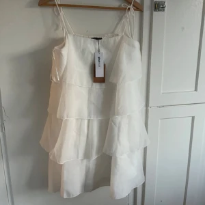 Studentklänning från Gina - Ny med lappen kvar!!! Säljer en söt vit klänning från Gina Tricot med flera lager volanger. Klänningen har smala axelband och en luftig passform, perfekt för varma dagar. Den är kort och ger en lätt och somrig känsla. Perfekt för en avslappnad stil. Perfekt till studenten!❤️Nypris är 700. Priset kan diskuteras 🥰