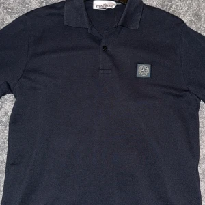 Mörkblå pikétröja från Stone Island - Säljer en stilren mörkblå pikétröja från Stone Island. Den är i nyskick samt aldrig använd, nypris är 1899. Tveka inte att höra av dig om du har några frågor eller funderingar. 
