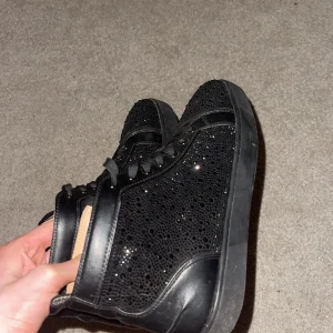 Svarta glittriga loubitins - Snygga svarta sneakers med glittrig yta och snörning. Perfekta för att ge en extra touch till din outfit. Skorna har en klassisk design med en modern twist tack vare det glittriga mönstret.