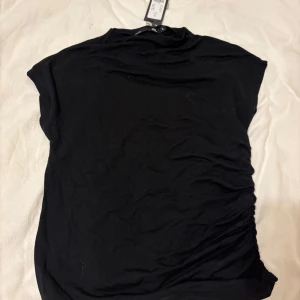 Svart kortärmad topp - Säljer en stilren svart kortärmad topp med en enkel design. Perfekt för en minimalistisk look. Toppen har en mjuk och bekväm passform.