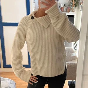  stickad tröja från Arket - Säljer en mysig beige stickad tröja från Arket i lammullsmix. Tröjan har en unik krage med knappdetalj och långa ärmar. 💕💕 Är i fint skicka och knappast använt den!