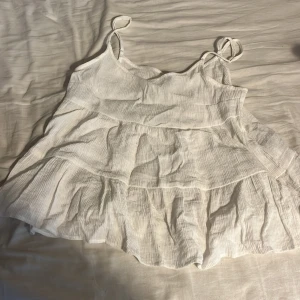 Vit volangtopp från Divided - Säljer en söt vit volangtopp från Divided. Toppen har tunna axelband och flera lager av volanger som ger en luftig och somrig känsla. Perfekt för varma dagar! 🌞 men tyvärr har en fläck som inte syns på kameran som ni ser på bilderna men ni ser typ inte för det syns inte❣️