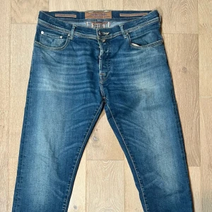 Jacob cohen jeans  - Snygga blå jeans från Jacob Cohen med klassisk femficksdesign och knappgylf. Jeansen har en lätt tvättad look och märkesdetaljer på baksidan. Perfekta för en avslappnad stil.