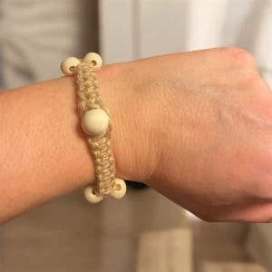 Beige armband med träpärlor - Charmigt beige armband knutet med makramé med jutesnöre och träpärlor i två storlekar. Armbandet har en justerbar kedja i silverfärg för perfekt passform. Perfekt för en naturlig och bohemisk stil.
