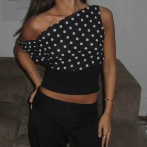 Svart prickig oneshoulder topp - Säljer en svart oneshoulder topp med vita prickar. Toppen har en bred ribbad midja och är croppad. Perfekt för dig som vill sticka ut med ett trendigt mönster och snygg passform.