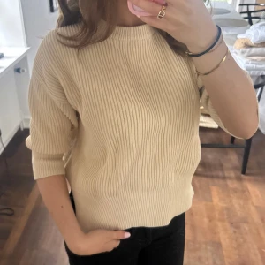 Beige ribbad stickad tröja från COS - Beige ribbad stickad tröja från COS med rund halsringning och trekvartsärm. Tröjan har en croppad passform och slits i sidan☺️