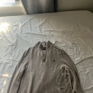 Beige merinoullströja med halv dragkedja från Morris - Säljer en stilren beige tröja från Morris i 100% merinoull. Tröjan har halv dragkedja framtill och en liten broderad logga på bröstet. Perfekt för lager-på-lager och passar till många olika outfits.