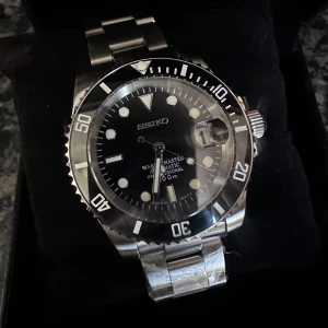 Seiko Marinemaster automatisk herrklocka - Säljer en Seiko Marinemaster automatisk klocka med svart urtavla och silverfärgat armband i metall. Klockan har tydliga index, datumfönster med förstoringsglas och vridbar bezel. Klassisk dykardesign och robust känsla.