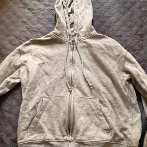 Grå hoodie med dragkedja från H&M Divided - Säljer en ljusgrå hoodie från H&M Divided i storlek XS. Tröjan har huva med dragsko, hel dragkedja framtill och två stora fickor. Perfekt för en avslappnad stil och enkel att matcha med det mesta. Hårfärgs fläck vid handen, ej testat behandla dock. Pris kan diskuteras