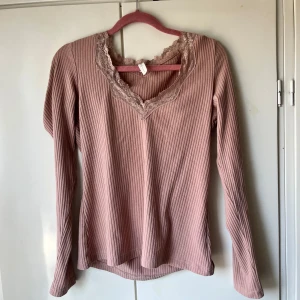 Rosa ribbad långärmad topp med spets - Säljer en ljusrosa ribbad topp med lång ärm och v-ringning dekorerad med spets. Påminde mycket om toppen från intimissmi. Perfekt för en liten söt touch på en basic outfit.