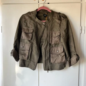 Mörkgrön utilityjacka från Lindex - Säljer en ”militärgrön” utilityjacka från Lindex med fyra stora fickor framtill och dragkedja. Jackan har axelklaffar och en rak passform. Perfekt för att kunna styla med alla basic färger och så snygg till sommarkvällar! 
