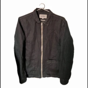 Elvine overshirt - Säljer en svart jacka från Elvine med klassisk krage och dragkedja framtill. Jackan har två stora fickor framtill och är i ett stilrent, enkelt snitt. Är i linne tyg och perfekt nu när det är vår för en fet stil! Tveka inte på att höra av er vid frågor.