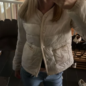 Krämvit quiltad pufferjacka från Gina Tricot i storleken 170 - Säljer en beige quiltad pufferjacka från Gina Tricot. Jackan har lång ärm, knappar framtill och två fickor. Den är kortare i modellen och har en stilren, enkel design som passar till många outfits.