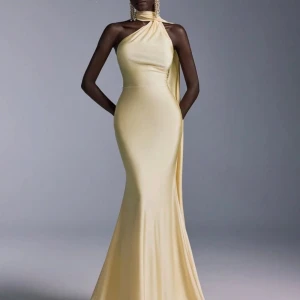 Ljusgul långklänning med oneshoulder - Elegant ljusgul långklänning med oneshoulder-design och figurnära passform. Klänningen har en lång, svepande kjol och en snygg detalj med tyg som faller från axeln ner längs ryggen. Perfekt för bal eller festliga tillfällen. Säljer då jag valde en annan till min bal.