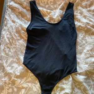 Svart ribbad body - Säljer en svart ribbad Badu med klassisk skärning och djup urringning både fram och bak. Enkel och stilren design som passar till många tillfällen.