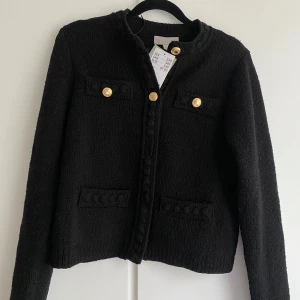 Svart cardigan jacka med guldknappar - Säljer en svart cardigan jacka med dekorativa guldknappar framtill och på fickorna. Jackan har rund halsringning, lång ärm och är tillverkad i ett stickat material. Perfekt för en stilren och klassisk look. Skulle säga att den passar S då den blev lite för stor för mig som bär xxs/xs