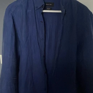 Mörkblå linneskjorta från Massimo Dutti - Säljer en stilren mörkblå skjorta i linne från Massimo Dutti. Skjortan har lång ärm och klassisk krage med knäppning framtill. Perfekt för en avslappnad men snygg look.