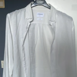 Vit linneskjorta från Lindbergh - Säljer en stilren vit skjorta från Lindbergh i luftigt linne. Skjortan har klassisk krage, knäppning framtill och långa ärmar. Perfekt för en fräsch och avslappnad look.