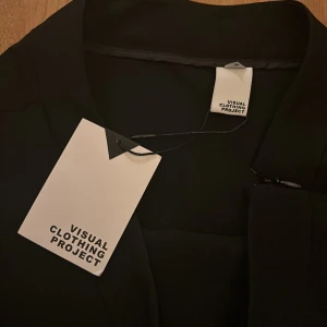Svart kjol med fransar från Visual Clothing Project - Säljer en svart kjol från Visual Clothing Project med snygga fransdetaljer längs nederkanten. Kjolen har en kort passform och är perfekt för dig som vill sticka ut med en trendig look.