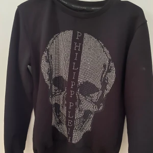 Philipp Plein tröja -  sweatshirt från Philipp Plein med ett stort döskalletryck i silver framtill. Tröjan har rund halsringning och långa ärmar. Perfekt för dig som gillar edgy streetstyle.