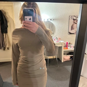 Beige långärmad klänning från Kappahl - Säljer en beige långärmad klänning från Kappahl med figurnära passform. Klänningen har en lätt glittrig yta och kan bäras både med båtringning och offshoulder. Materialet är mjukt och stretchigt, klänningen är aldrig använd. klänningen är en kortklänning. 