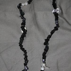 Svart halsband med pärlor från SNÖ - Unikt halsband från SNÖ med svarta fyrkantiga pärlor och inslag av vita pärlor. Snygg detalj med märkets logga på en liten silverbricka. Perfekt accessoar för att lyfta din outfit.