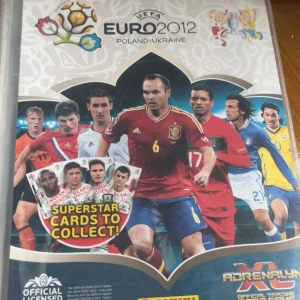 UEFA Euro 2012 Adrenalyn XL samlarkortbok - Säljer en samlarkortbok från UEFA Euro 2012 Adrenalyn XL, officiellt licensierad av Panini. Boken innehåller fotbollssamlarkort med spelare från olika europeiska landslag, bland annat Spanien, Tyskland, Sverige, Portugal och Polen. Perfekt för samlare av fotbollskort. Korten är blandat av EM 2012 och Champions League. varje kort är värt mellan 15-30 kr och det är 90 kort därav priset