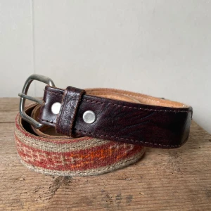 Bälte med vintage Kilim  - Unikt bälte med bred, mönstrad Kilim matta i beige, rött och orange samt mörkbrunt skinn vid spännet. Bältet har ett klassiskt metallspänne och insida i ljust mjukt skinn. Perfekt för att ge outfiten en personlig touch. Lite tecken på användning.