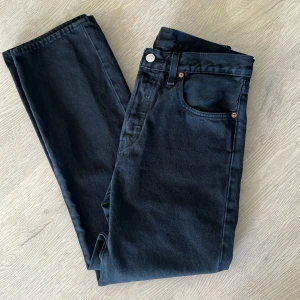 Svarta Levi's 501 jeans W31 L30 - Klassiska svarta Levi's 501 jeans med raka ben och fem fickor. Byxorna har knappgylf, läderpatch bak i midjan och den ikoniska röda Levi's-taggen på bakfickan. Modellen är W31 L30 och passar perfekt till en avslappnad stil.