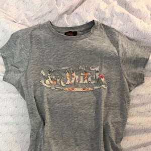 Von Dutch Tshirt med blommigt tryck - Grå t-shirt från Von Dutch med ett stort blommigt Von Dutch-tryck på bröstet. Klassisk rund halsringning och korta ärmar. Perfekt för en avslappnad och trendig stil.