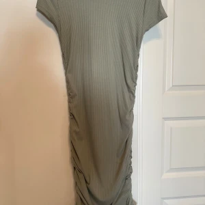 Grå ribbad klänning - Säljer en grå ribbad klänning med korta ärmar och rund halsringning. Klänningen har en rak passform och är rynkad längs sidorna vilket ger en snygg detalj. Perfekt för dig som gillar enkel men stilren design. Klänningen är använd max 2 gånger.