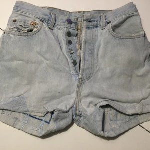 Ljusblå jeansshorts Levis med patchwork - Unika ljusblå jeansshorts från Levi's med synliga patchwork-detaljer och knappar framtill. Klassisk femficksmodell med hög midja. Levis, vet ej modell Uppskattad storlek 29, midja 80 cm Lappade, med gylf
