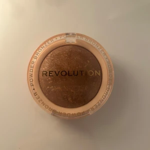 Revolution Bronzer Reloaded Long Weekend - Revolution Bronzer Reloaded i nyansen Long Weekend. Det är ett pressat puderbronzer med en varm, gyllene ton och lätt skimrig finish. Förpackningen är öppnad och bronzern är bara testad en gång. 