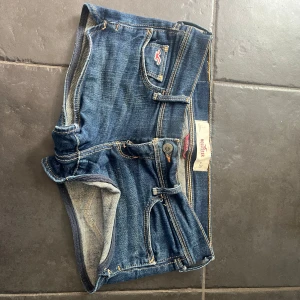 Mörkblå jeansshorts från Hollister - Snygga mörkblå jeansshorts från Hollister med klassiska fickor och kontrastsömmar. Modellen är kort och har låg midja samt en liten broderad logga framtill. Perfekt  för varma dagar och enkelt att matcha till! 