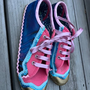 Färgglada sneakers med paljettdetaljer från PRGO - Unika sneakers i blått och rosa med glittriga paljetter, rosa snörning och guldiga tår. Sulan är dekorerad med stjärnmönster och insidan har blommigt tyg. Perfekta för dig som gillar färg och detaljer! Designade i Sevilla, Spanien. 