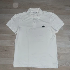 VIT PIKÉ FRÅN LACOSTE - Säljer en stilren vit piké från Lacoste. Pikén är väldigt simpel men väldigt snygg och perfekt för dig som söker en för sommarn. Storleken är S. Skriv gärna vid minsta fråga, pris kan diskuteras. Nypris 1000kr