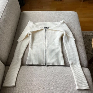 Vit kofta från Gina Tricot - Säljer en vit ribbad och mjuk kofta från Gina Tricot med 2 dragkedjor framtill och bred krage som kan vikas ner. Tröjan har lång ärm och är figurnära i modellen. Perfekt att styla till olika outfits!