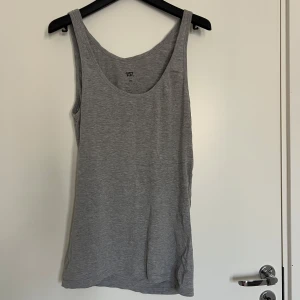 Grått baslinne - Säljer ett enkelt grått linne med rund halsringning. Perfekt att ha som basplagg till olika outfits. Mjukt material och klassisk passform.