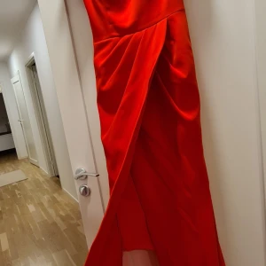 Röd långklänning med puffärm och slits - Snygg röd långklänning med puffärmar och markerad midja. Klänningen har en elegant slits framtill och draperade detaljer som ger en lyxig känsla. Perfekt för speciella tillfällen när du vill sticka ut. Användt bara en gång 